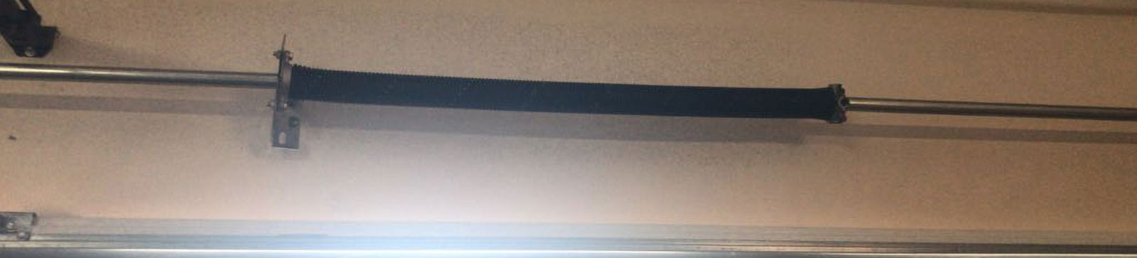 Close-up of a visibly broken torsion spring above a sectional garage door in a Chicago, IL home.